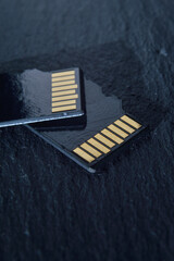 two micro sd cards lie on top of each other on a dark textured background, with golden contacts at...