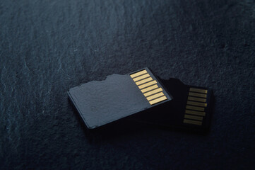 two micro sd cards lie on top of each other on a dark textured background, with golden contacts at...