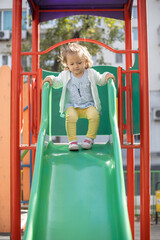 Little girl having fun on outdoor playground. On slide
