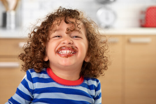 Portrait of laughing toddler with curly hair and chocolate mustache