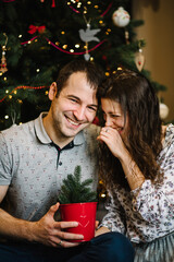 Man and woman laughing during winter holidays. Happy couple in love sitting on the floor near the Christmas tree. Happy New Year and Merry Christmas.
