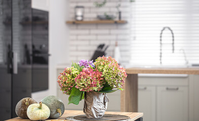 A bouquet of hydrangeas and pumpkins on the kitchen table as part of autumn home decor.