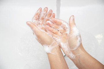 Fototapeta premium Close up a woman is washing soap foam from her hands under running water.