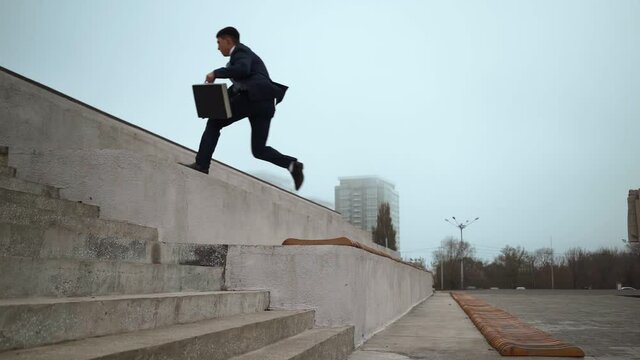 Young businessman in suit with black briefcase in his hands jumps up the parapets against city background. Business success teamwork concept. Career ladder concept. Corporate promotion. Slow motion.