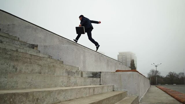 Young businessman in suit with black briefcase in his hands jumps up the parapets against city background. Business success teamwork concept. Career ladder concept. Corporate promotion. Slow motion.