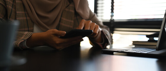 Cropped shot of muslim woman hand typing on mobile phone while sitting at her workplace.