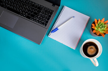 Workplace in the home office on a blue background. Top view of a part of a laptop with a Notepad, pen, glasses, plant and coffee. The concept of business and investment.