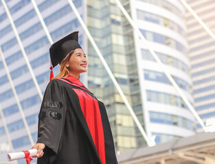 Asian  graduated women in graduation gowns , holding diploma, open arms, smiling and looking up....