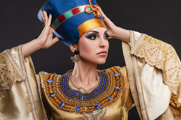 closeup studio portrait of a beautiful woman with brown eyes and evening make-up in the image of Queen Cleopatra, crown, necklace, golden dress - obrazy, fototapety, plakaty