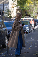 Obraz premium Young woman in a fashionable long coat walks in autumn city. copy space