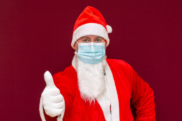 Fototapeta na wymiar Closeup selective focus Santa Claus wearing medical mask shows thumb up New year and Merry Christmas concept.