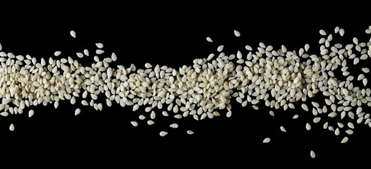 Sesame seeds arranged in row, line isolated on black background, top view