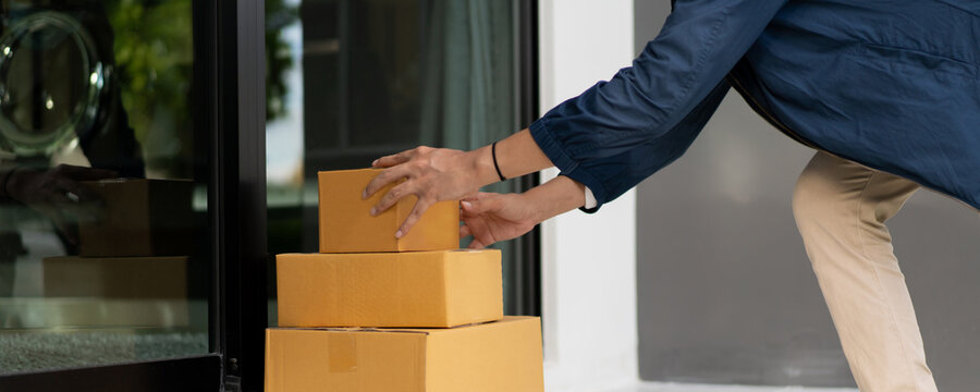 Asian postman with a hygiene protective face mask picking up a parcel package or parcel box from the truck for deliver to customer's door. 