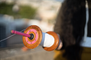 slow motion shot of thread being pulled quickly from charkhi spool as an out of focus person in the background flies the kite and takes the kite higher and farther