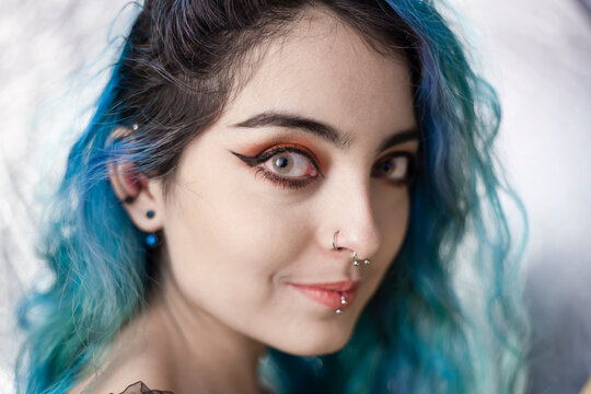 Portrait of young alternative model with make up, eyeliner, pale skin, piercings, contact lenses and blue dyed hair  looking to the camera with a cute and calm expression. Feminism and empowerment.