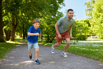 family, fatherhood and people concept - happy father with little son compete in running at summer...
