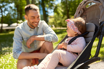 family, fatherhood and people concept - happy father with child in stroller at summer park