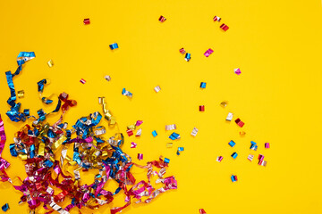 Colorful bright confetti and streamers on yellow background, top view. Copy space for text. Holiday mood, Christmas, New year, birthday or funny party