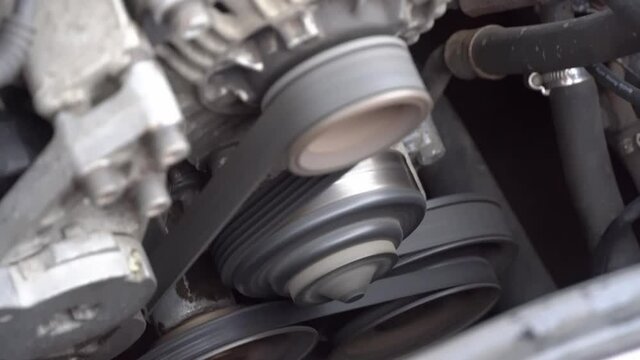 The car engine is running. Close-up rotation of parts, belt, generator and pulleys on the car engine.