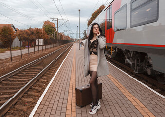 young girl in gray coat with suitcase standing at railway station