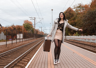 young girl in a gray coat with a suitcase walks along the railway station