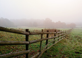 Fototapeta premium wooden fence between fields in the fog