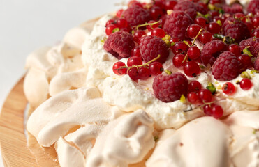 food, culinary, baking and cooking concept - close up of pavlova meringue cake decorated with red berries on wooden serving board