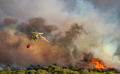 Rauch und riesiger Feuerhintergrund und Hubschrauber mit Bambi-Eimer