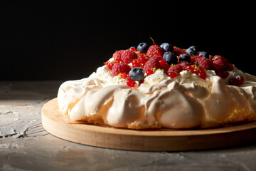 food, culinary, baking and cooking concept - close up of pavlova meringue cake decorated with berries on wooden serving board
