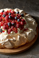 food, culinary, baking and cooking concept - close up of pavlova meringue cake decorated with berries on wooden serving board