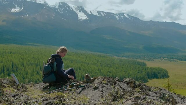 A lonely young woman building a pyramid of rocks on top. Meditation and relaxation in the fresh air while hiking through the picturesque mountains.