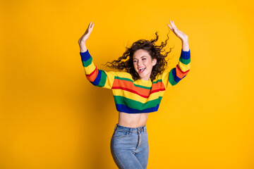 Photo of adorable sweet lady wearing casual colorful sweater dancing looking empty space hands arms up isolated yellow color background