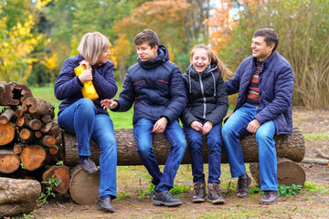 family relaxing outdoor in autumn city park, happy people together, parents and children, they drink tea, talking and smiling, beautiful nature