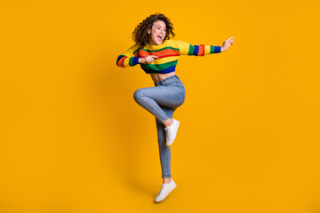 Fototapeta na wymiar Full length photo of jumping lady wearing casual colorful sweater dancing pointing looking empty space standing one leg isolated yellow color background