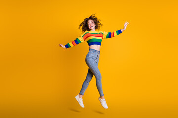 Fototapeta na wymiar Full length photo of shiny jumping woman dressed casual colorful sweatshirt hands arms side isolated yellow color background