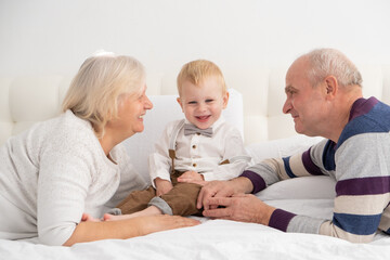 Happy good looking senior couple husband and wife with their adorable grandson on bed. 