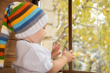 baby boy in a colored hat looks out the window.