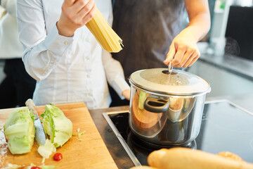 Friends prepare spaghetti noodles for cooking for lunch