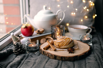 A cup of hot tea with lemon in an early winter morning by the window. Knitted wool warm blanket, hot homemade apple cakes with cinnamon and star anise . Decor. Home winter holiday concept.