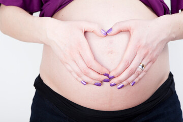 Pregnant women holding her hands heart shaped on her belly. Studio portrait isolated on white background.
