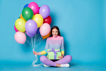 Fototapeta na wymiar Full length photo of pretty girl sit floor legs crossed hold balloons gift box wear pullover isolated blue color background