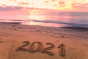 Inscription 2021 written on the sandy beach with a wave. Happy New Year concept