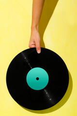 Woman holding vintage vinyl record against bright yellow background