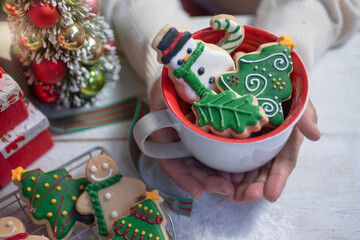 Woman holding a cup of Christmas cookies and festive decor on wooden table, selective focus