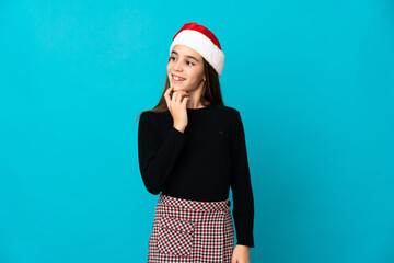 Little girl with Christmas hat isolated on blue background looking up while smiling