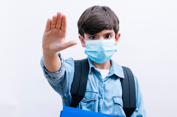 Handsome child boy student with backpack and mask holding books on isolated white background with open hand making stop sign