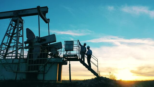 Two oil workers inspecting an oil field at bright sunset