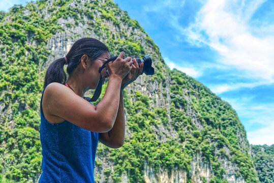 Side low angle view tourist asian woman wear blue undershirt and take photo with beautiful background mountain and blue sky.
