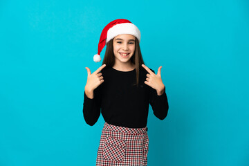 Little girl with Christmas hat isolated on blue background giving a thumbs up gesture