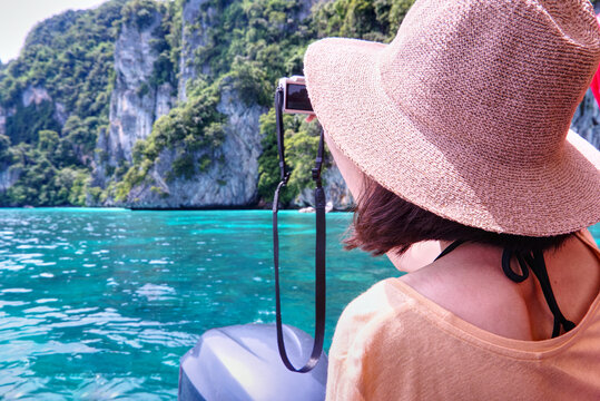 View from back tourist wear straw hat and take photo with background beautiful sea landscape and mountain
